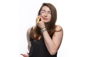 woman in black top and jeans applies eye make up with a brush